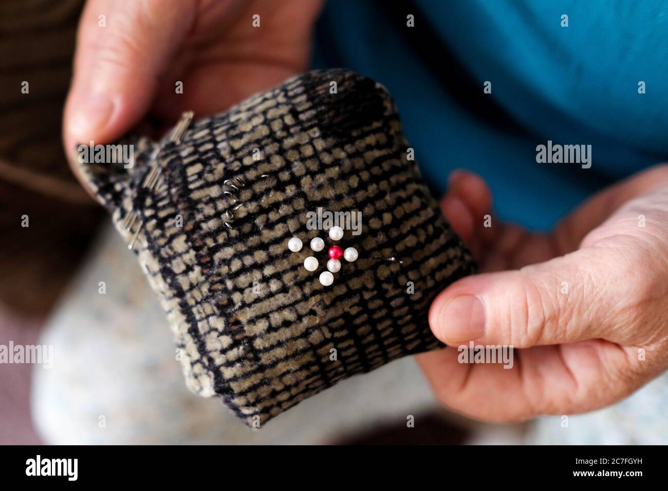 Weiche Matte zum Nähen von Nadeln. Die älteren Hände der Näherin halten das Werkzeug. Blick von oben. Stockfoto