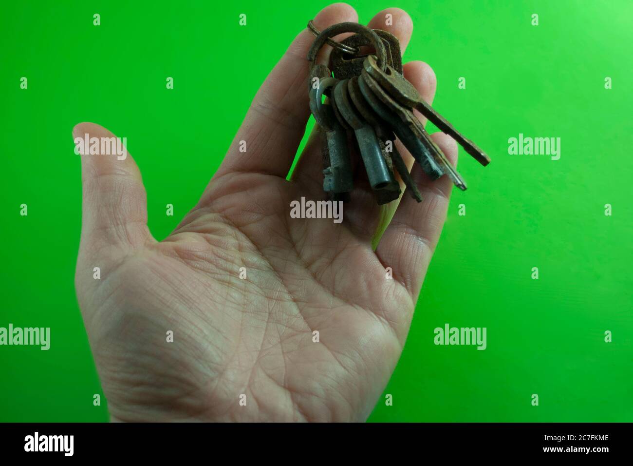 Zeigt eine Hand mit einer Schnur von Schlüsseln, die von zwei Metallringen auf einem grünen Hintergrund gebunden sind Stockfoto