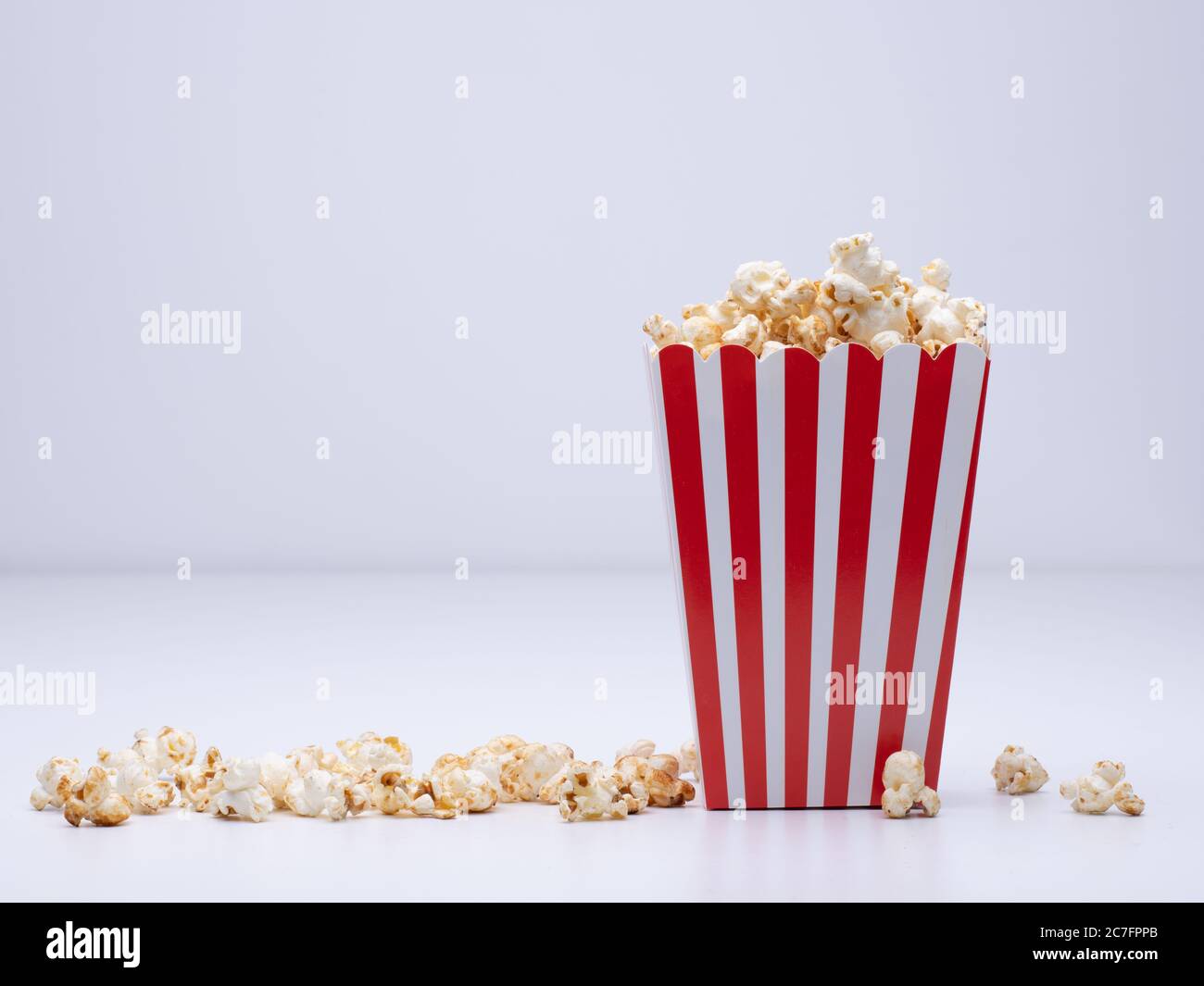 Papierbecher Popcorn und etwas Popcorn verstreut Eine weiße Oberfläche Stockfoto
