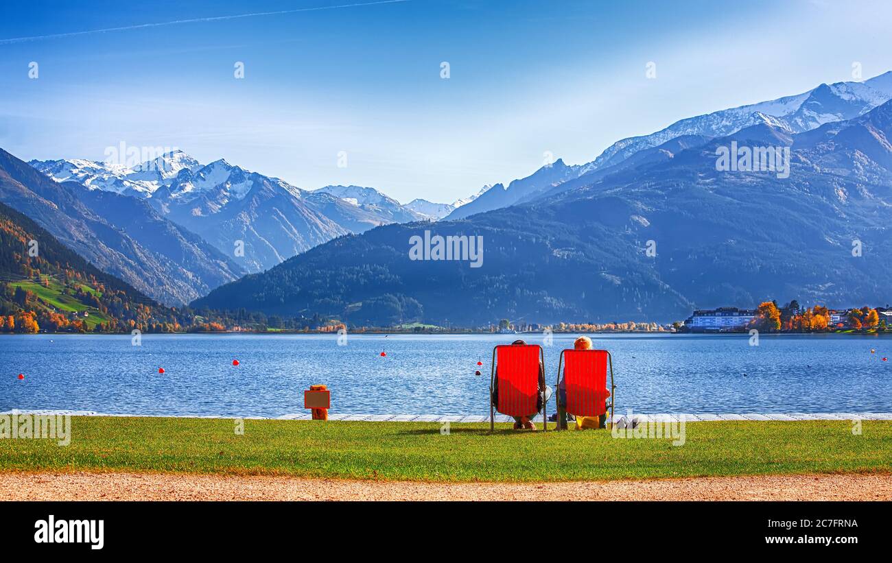 Spektakuläre Herbstansicht des Sees und Paar auf Stühlen sitzen in der Stadt Sell am See.. Fantastischer sonniger Tag über dem See. Ort: Zell am See, Salzburger Stockfoto