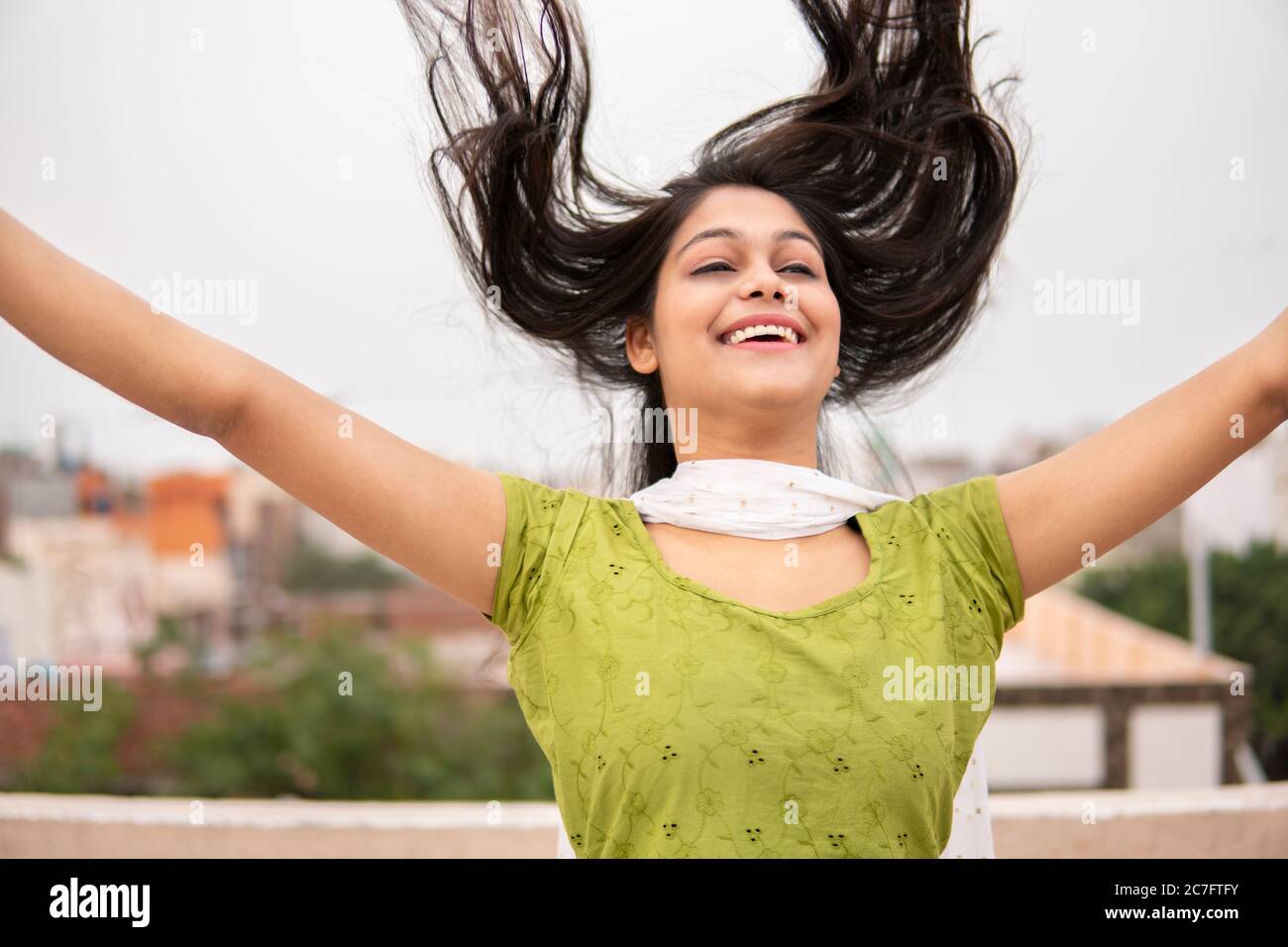 Schöne, glückliche indische spät teen Mädchen werfen Haare in der Luft und genießen frische Luft im Freien. Sie schaut auf und lächelt. Stockfoto