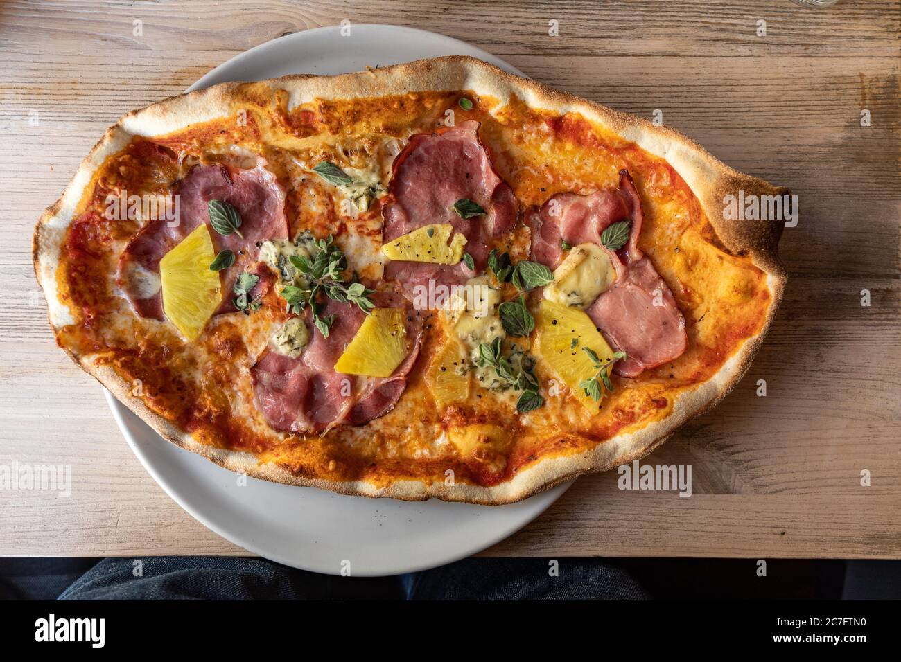 Ovale Pizza mit geräuchertem Schweinehals, Ananas und Blauschimmelkäse Stockfoto