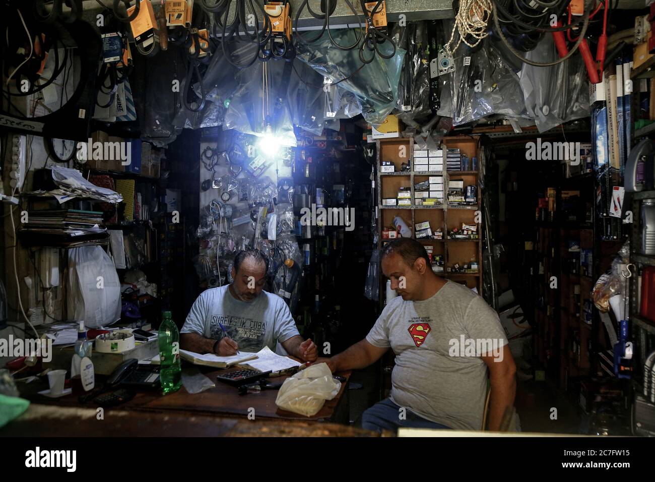 Beirut, Libanon. Juli 2020. Zwei Männer sitzen in einem Ersatzteilladen, der mit einer kleinen Glühbirne aufgehellt wurde, die während eines Stromausfalls, der manchmal 22 Stunden am Tag dauert, von einem privaten Generator in der Nähe genommen wurde. Quelle: Marwan Naamani/dpa/Alamy Live News Stockfoto