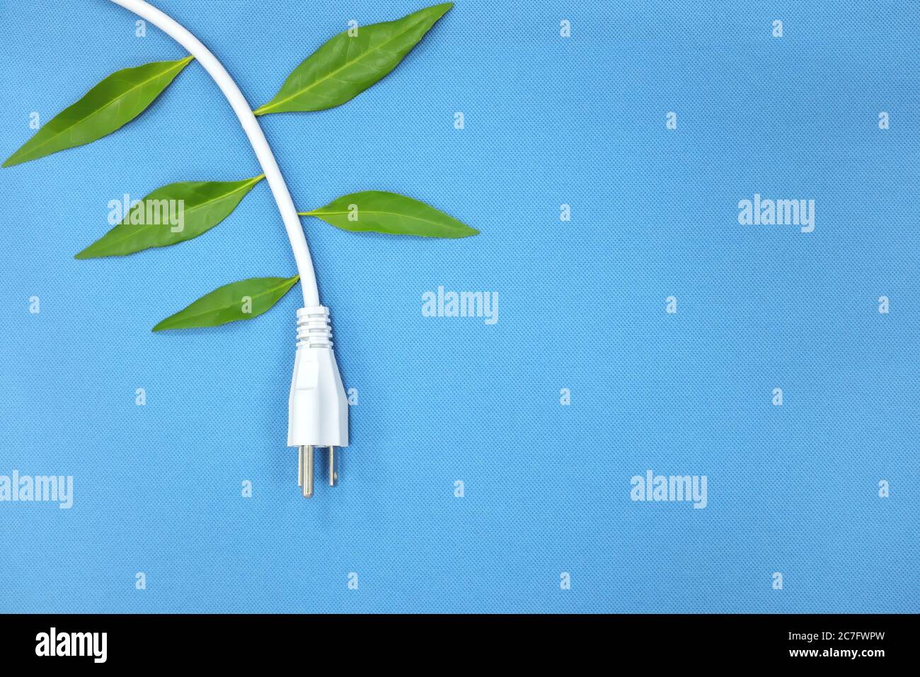 Elektrischer Stecker mit wachsenden grünen Blättern auf blauem Hintergrund. Sparen Sie Strom und alternative Energie Konzept. Stockfoto