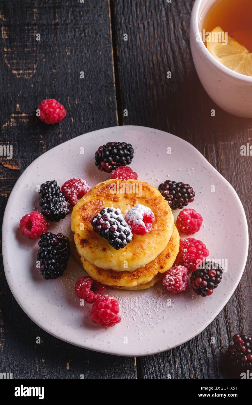 Quark Pfannkuchen, Quark Fritters Dessert mit Himbeere und Brombeere Beeren in Platte in der Nähe von heißen Teetasse mit Zitronenscheibe Stockfoto