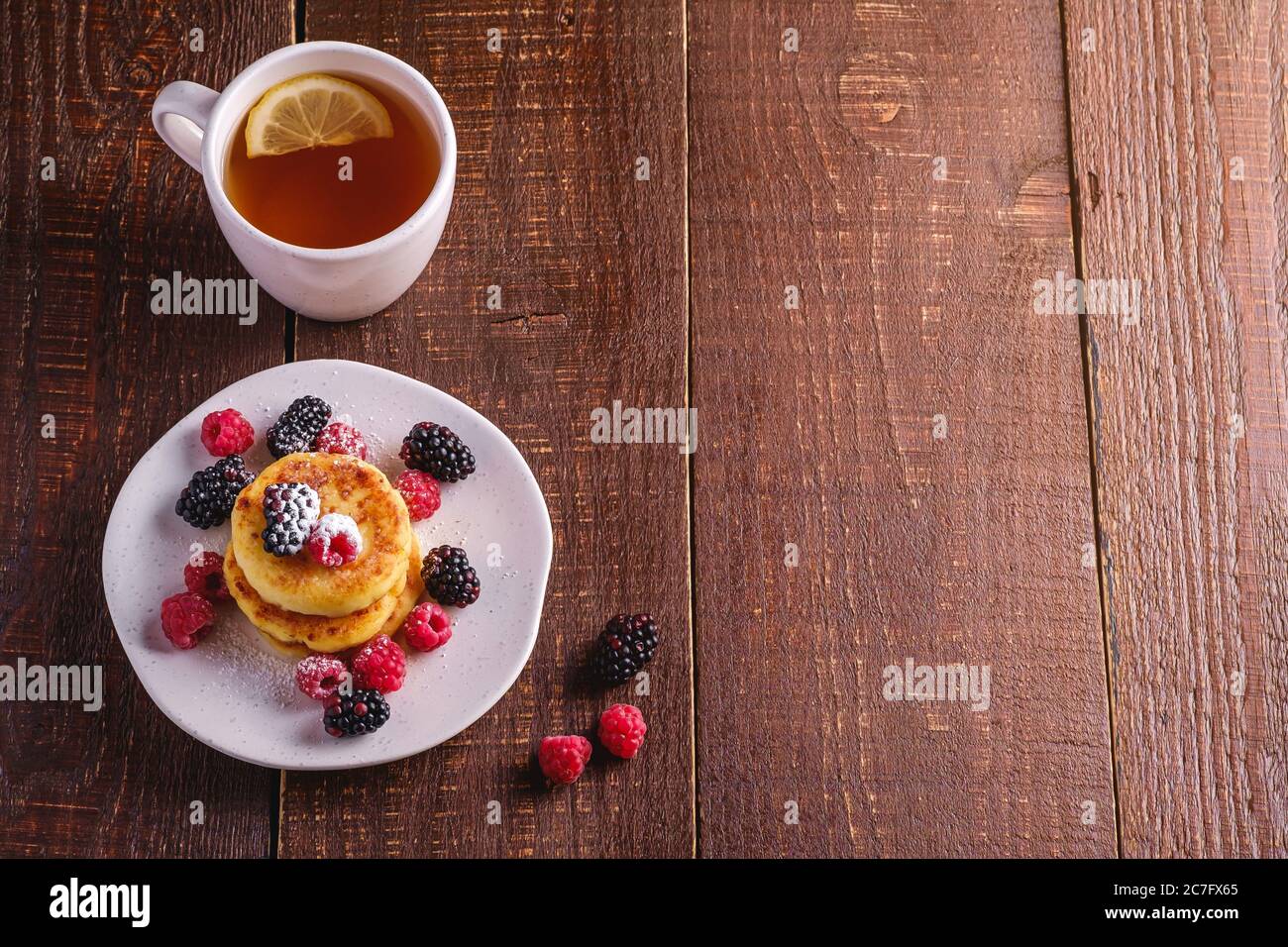 Quark Pfannkuchen, Quark Fritters Dessert mit Himbeere und Brombeere Beeren in Platte in der Nähe von heißen Teetasse mit Zitronenscheibe Stockfoto