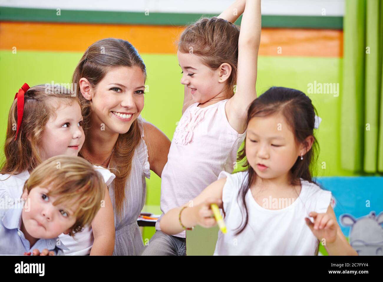 Lächelnder Erzieher spielt mit vielen Kindern im Kindergarten Stockfoto