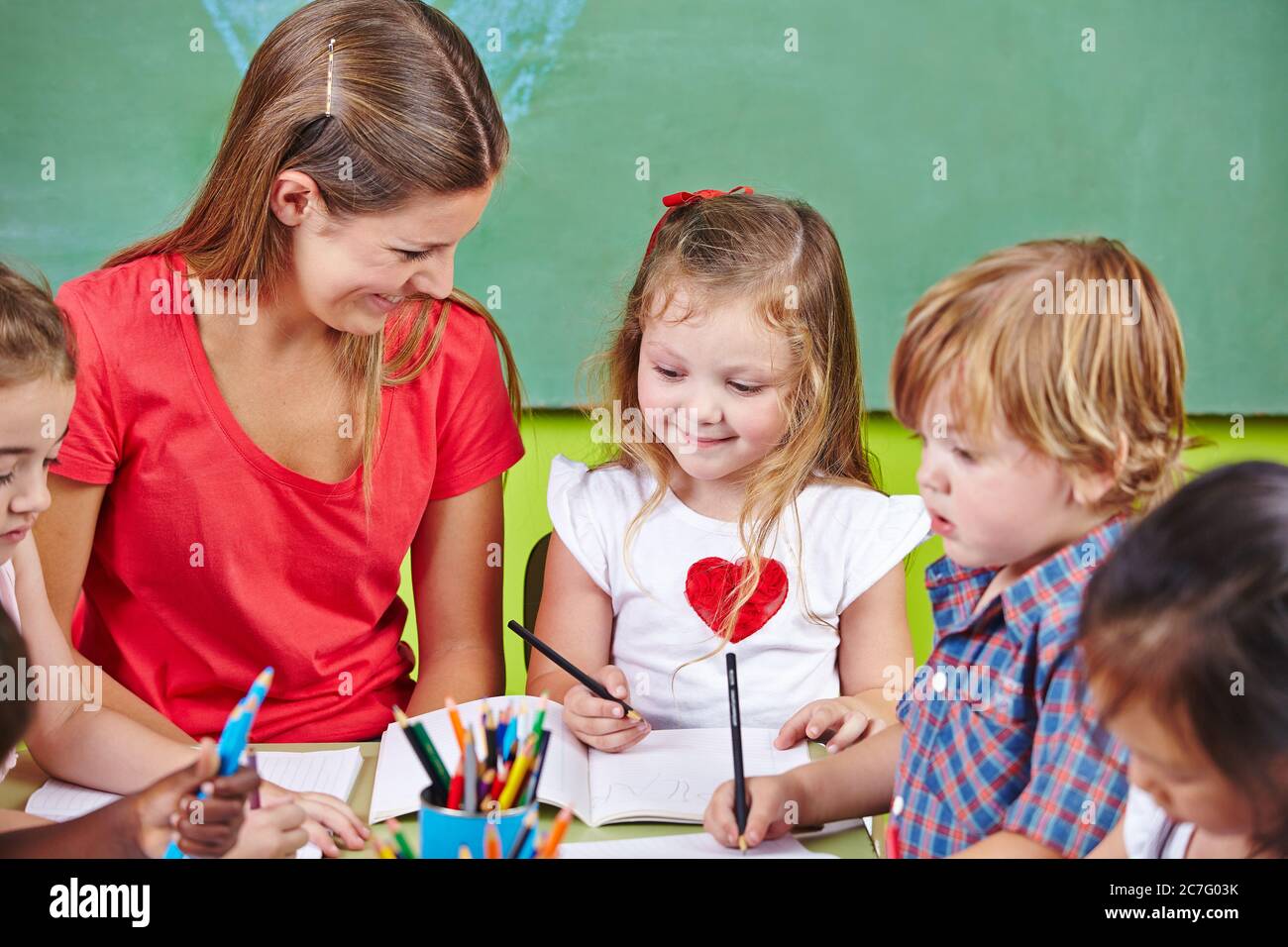 Einige Kinder malen zusammen mit einem lachenden Erzieher im Kindergarten Stockfoto