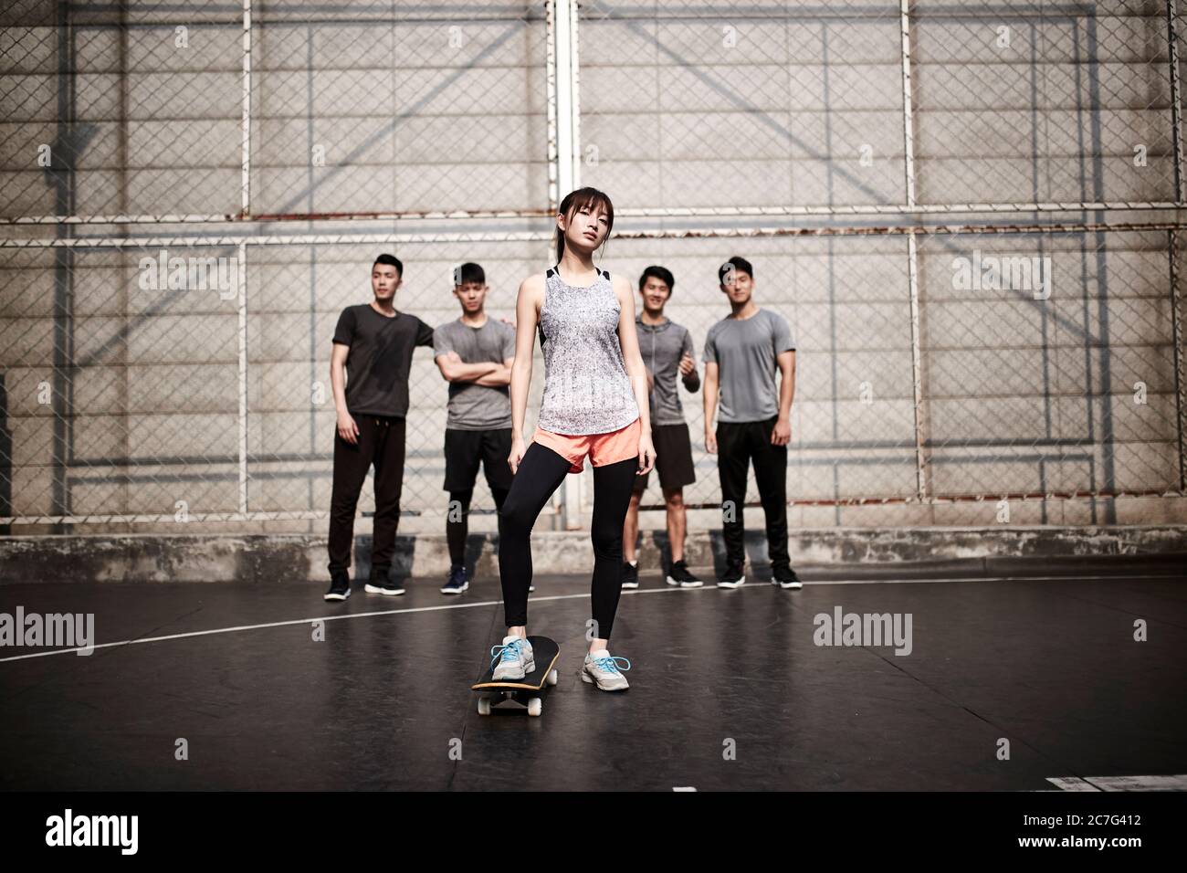 Hipster junge asiatische Frau posiert im Freien mit Skateboard und vier männlichen Freunden Stockfoto