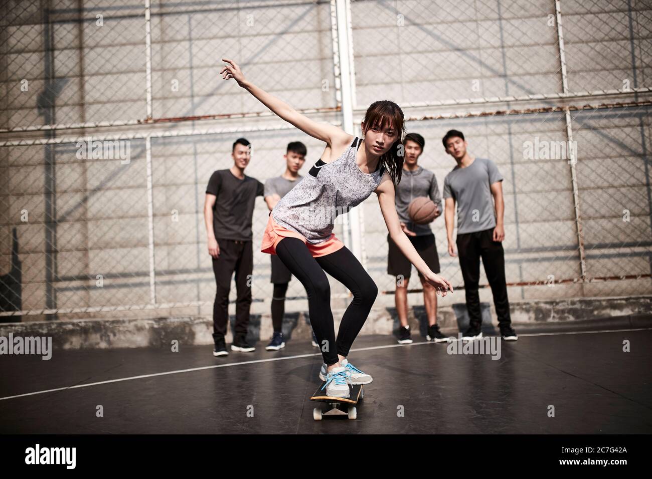 Junge asiatische Frau Skateboarder Skateboarding im Freien mit Freunden beobachten von hinten Stockfoto
