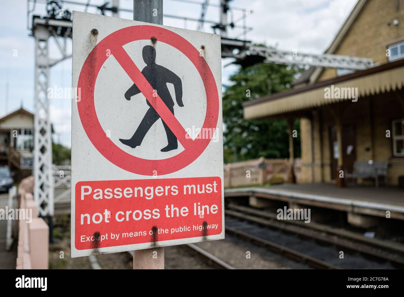 Nahaufnahme eines Metallwarnschildes für Passagiere, nicht um die Eisenbahnstrecke zu überqueren. Der Hintergrund zeigt einen verwagschwerten Bahnhof. Stockfoto
