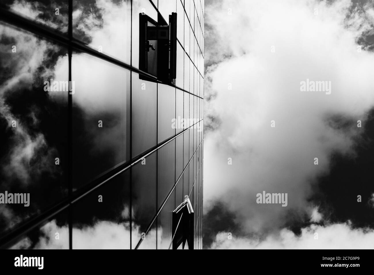 Graustufenaufnahme eines Glasturm, der das schöne reflektiert Wolken Stockfoto