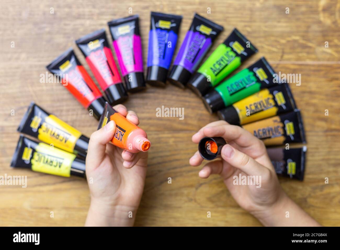 ZAGREB, KROATIEN - 17. Dez 2019: Kinderhände halten orangene Acrylfarbe über alten braun gealterten Holzplatten und bunte Acrylfarbe. Stockfoto
