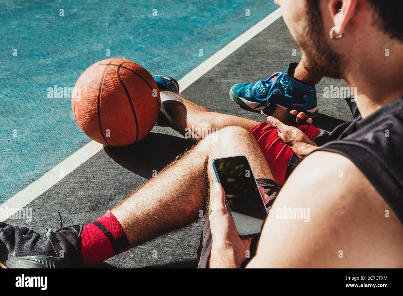 Der junge Mann ruht nach dem Basketballspiel und nutzt sein Smartphone mit seinem Freund Stockfoto