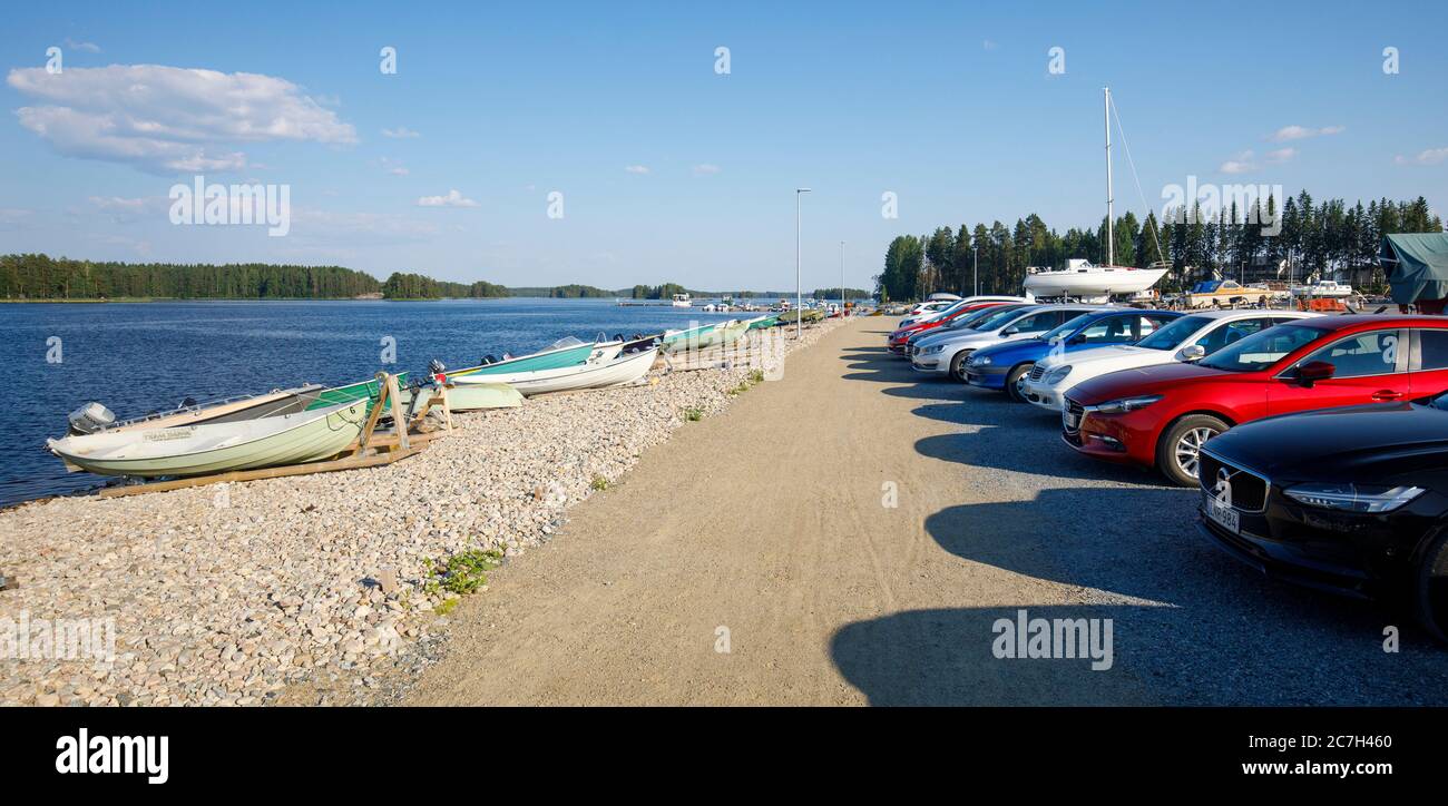 Autos am Seeufer geparkt und kleine Motorboote / Skiffs in Pirttilahden venesatama (Pirttilahti Marina) im Sommer, See Kallavesi, Kuopio, Finnland Stockfoto