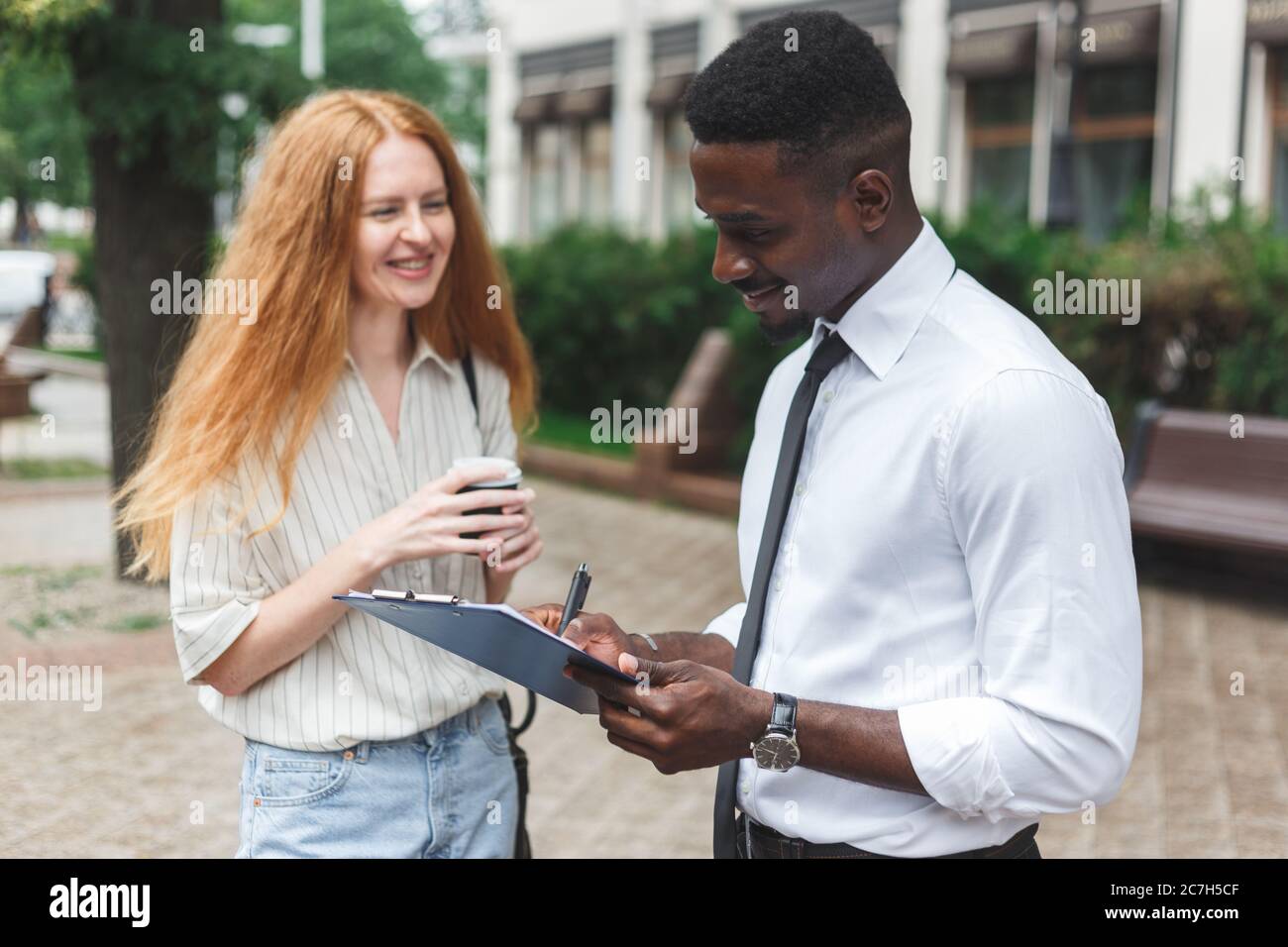 Schwarzer afroamerikanischer Mann auf der Straße, der eine Umfrage zu rothaariger Frau macht Stockfoto