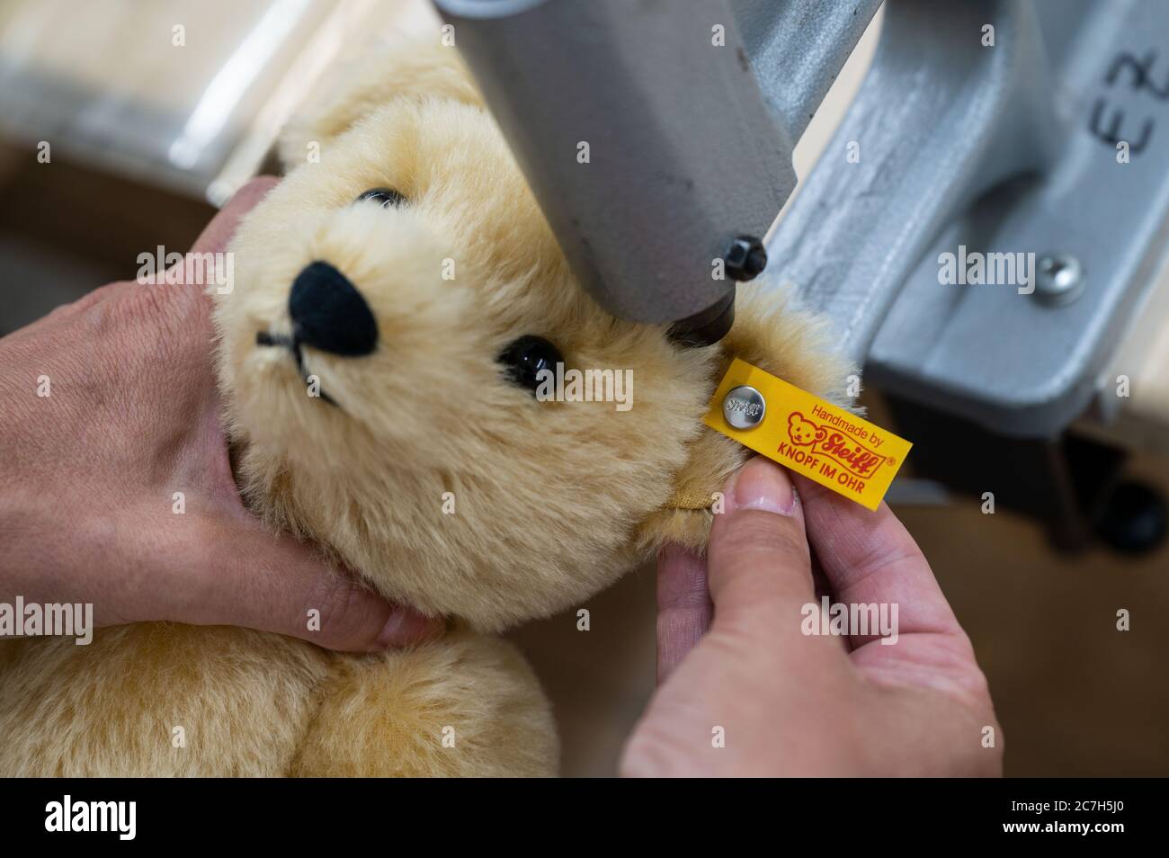 Giengen An Der Brenz, Deutschland. Juli 2020. Ein Mitarbeiter in der  Produktionsabteilung der Margarete Steiff GmbH bringt einen "Knopf im Ohr",  das Markenzeichen der Steiff Tiere, an ein Plüschtier an. Quelle: Marijan