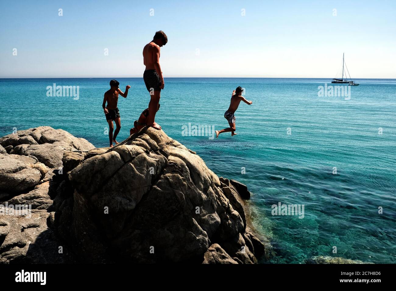 Blick auf eine Gruppe von Kindern, die von den Felsen am Strand von Limone in der Nähe von Villasimius in Sardinien, Italien, tauchen Stockfoto
