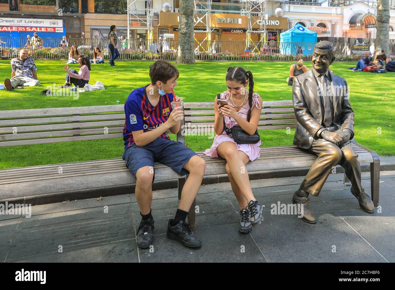 London, Großbritannien. Juli 2020. Die Menschen genießen eine Erfrischung neben der Mr. Bean Statue auf Leicester Square. Das West End wird langsam geschäftiger, wenn die Menschen in die Geschäfte und Parks im Zentrum Londons in der Sonne zurückkehren. Kredit: Imageplotter/Alamy Live Nachrichten Stockfoto
