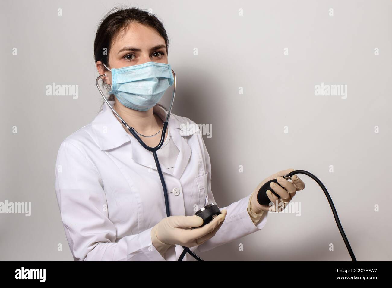 Arzt in einer medizinischen Maske misst der Kardiologe den Blutdruck mit einem Blutdruckmessgerät. Stockfoto