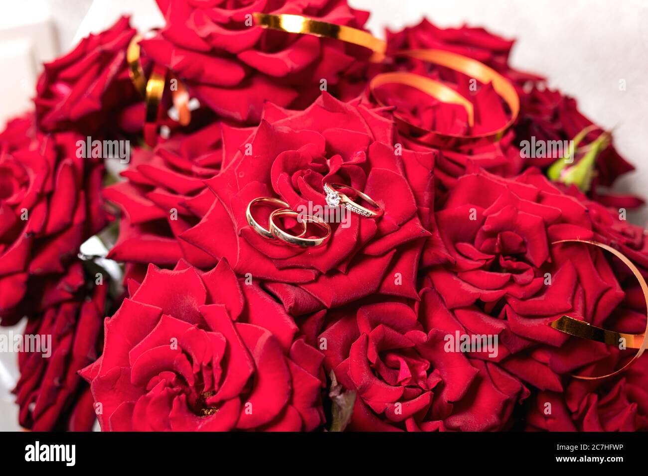 Goldene Eheringe auf einem Strauß roter Rosen Stockfoto
