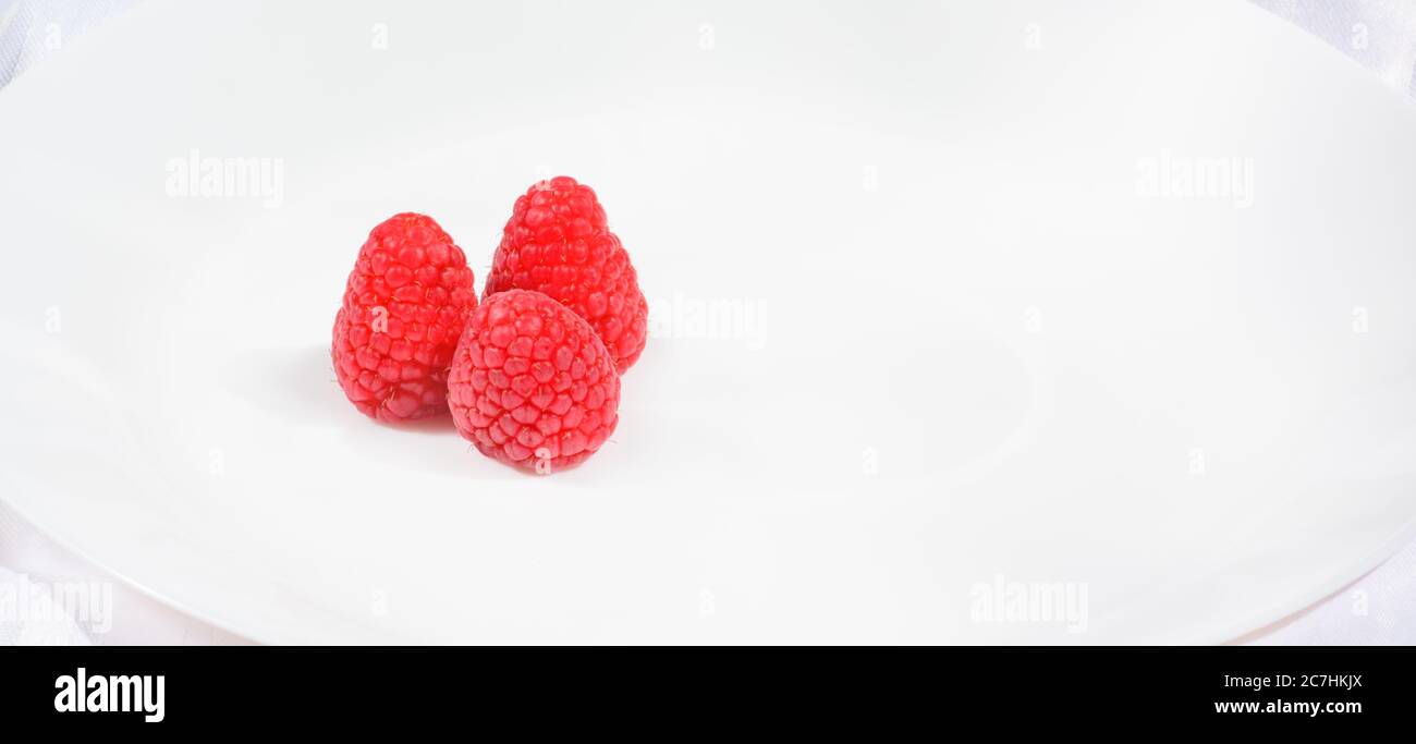 Drei Himbeeren auf einem weißen Teller im horizontalen Format Stockfoto