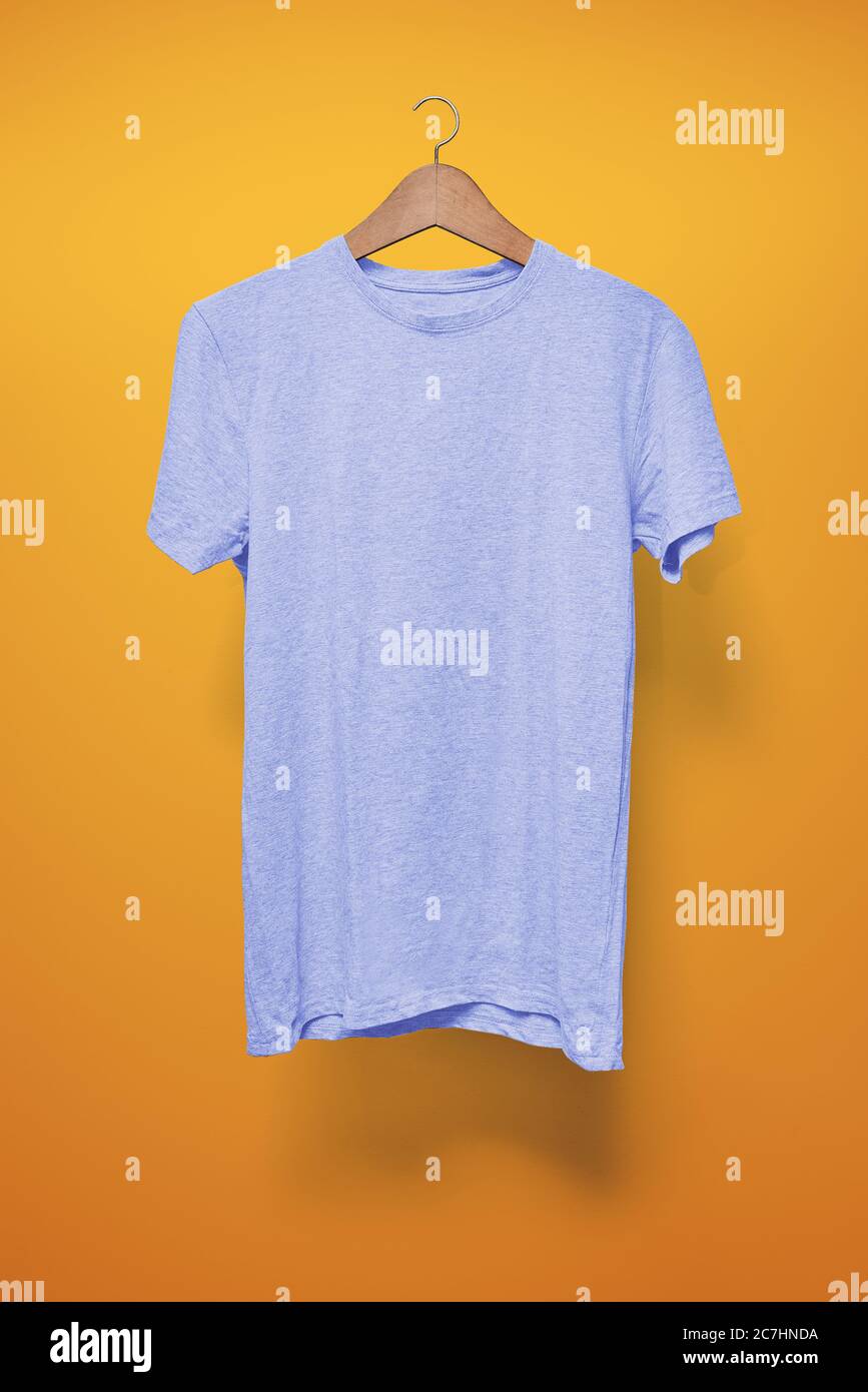 Hellblaues T-Shirt auf einem Kleiderbügel vor einem orangen Hintergrund Stockfoto