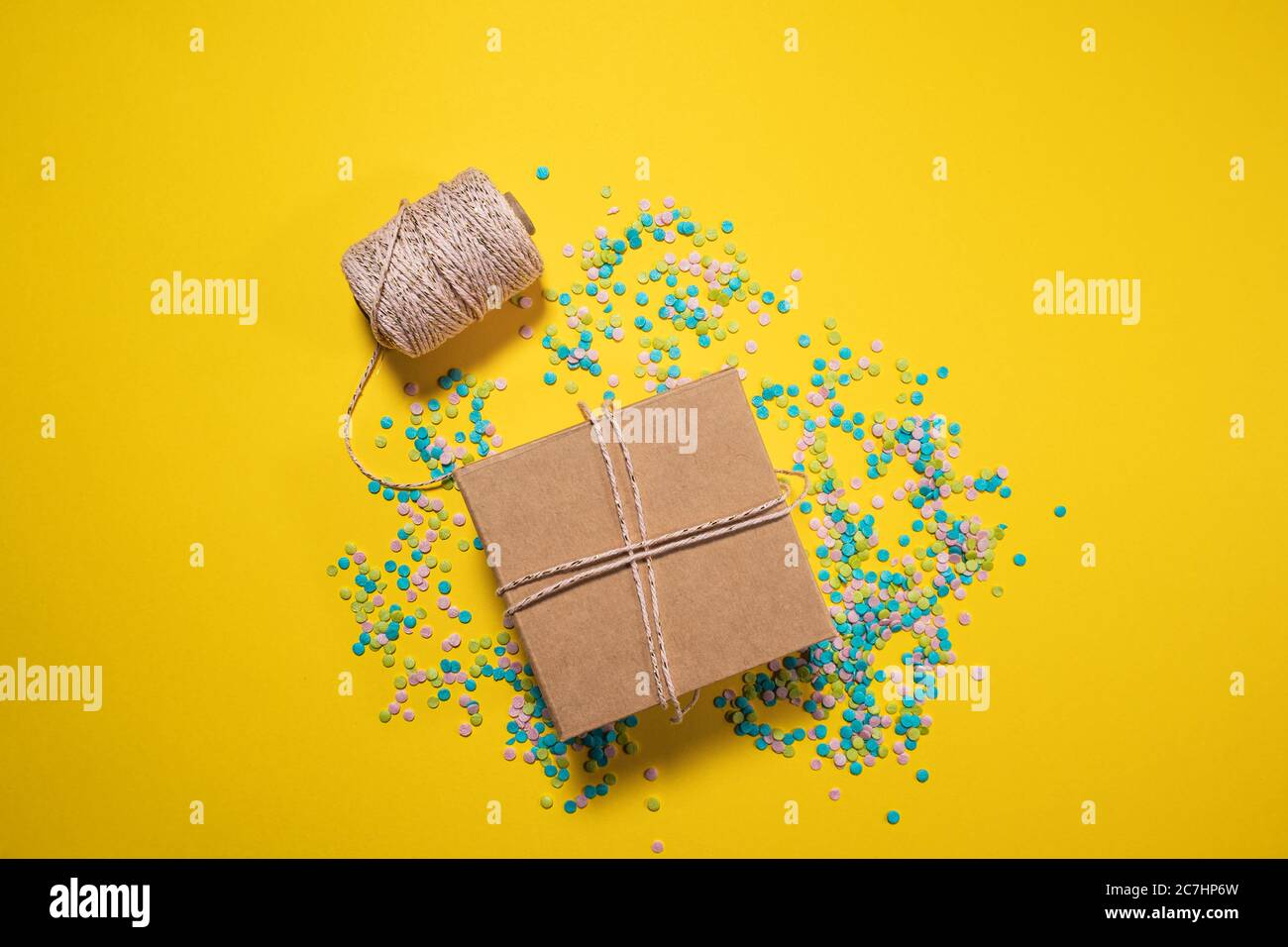 Geschenkbox in rosa Draht und Konfetti um sie gewickelt, gelb hellen Hintergrund, Geburtstagsgeschenk, Grußkarte Stockfoto