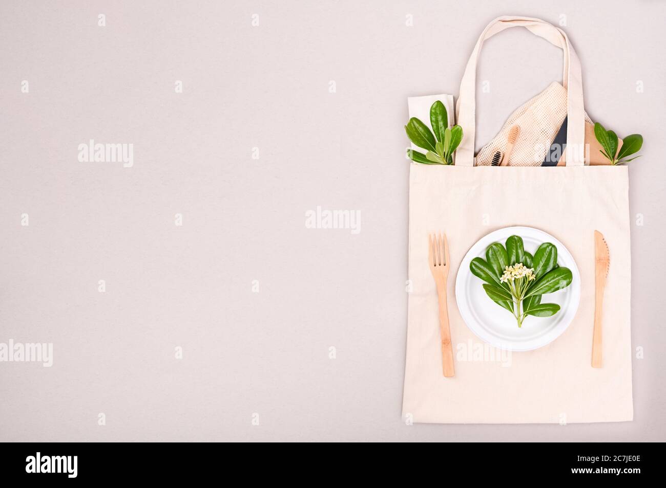 Stofftasche zum Einkaufen, auf grauem Hintergrund. Öko Haushaltswaren. Das Konzept des Recycling und der wiederverwendbaren Verwendung. Grundriss Grüne Blätter, Bambusbürsten, Papierutensilien, Gabel, Messer. Freier Speicherplatz für Text. Draufsicht Stockfoto