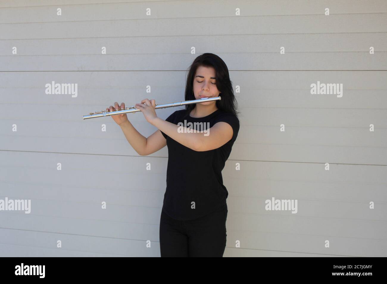 Schwarz-haarige Mädchen spielt die Flöte draußen vor einem weißen Hintergrund Stockfoto