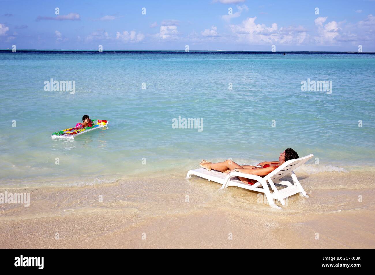 Mutter sonnenbaden, Tochter spielen mit einer aufblasbaren Matratze am Strand Gulhi, Malediven Stockfoto