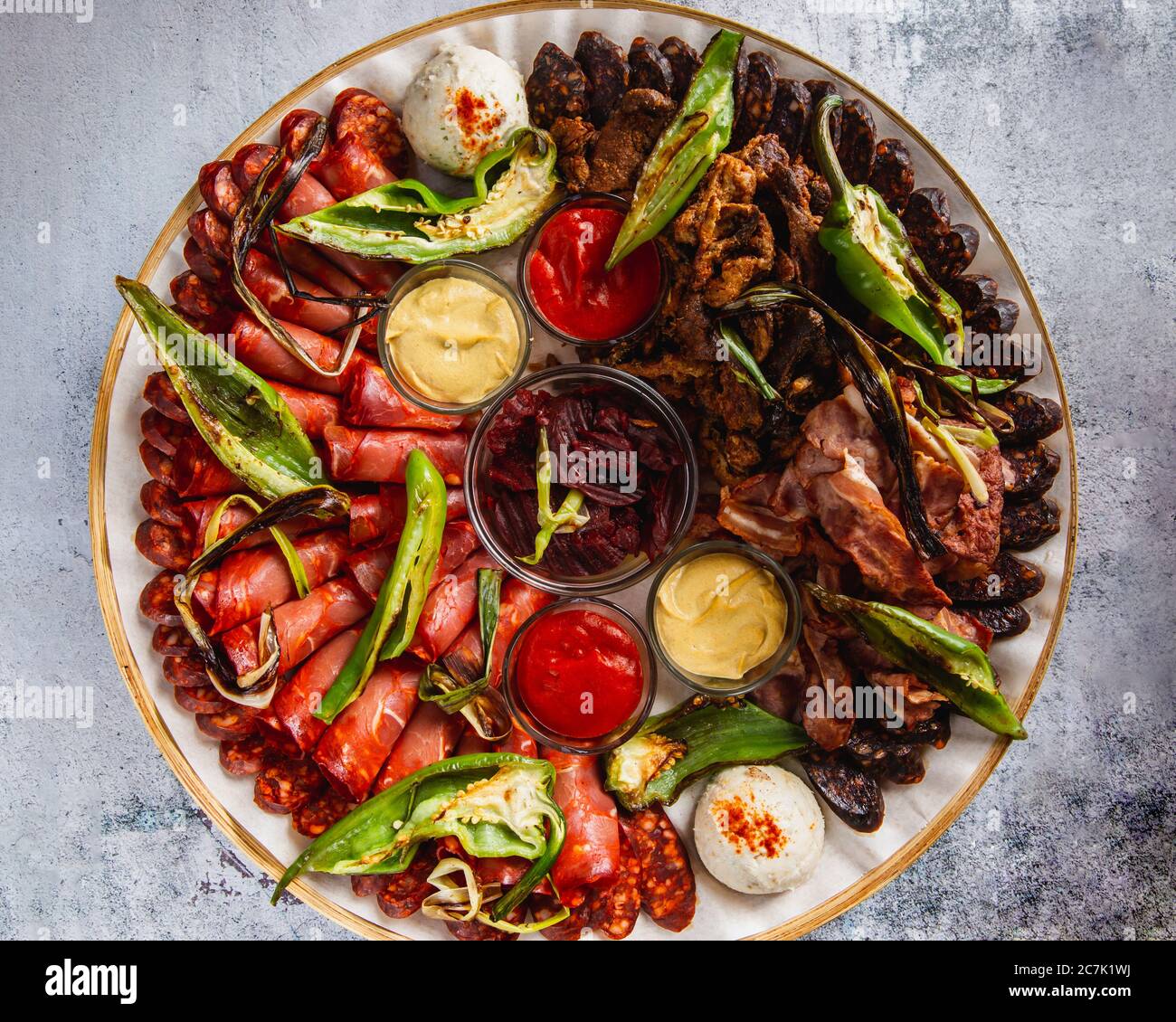 Verschiedene Fleisch- und Wurstsorten sowie gegrilltes Gemüse auf einem runden Teller Stockfoto