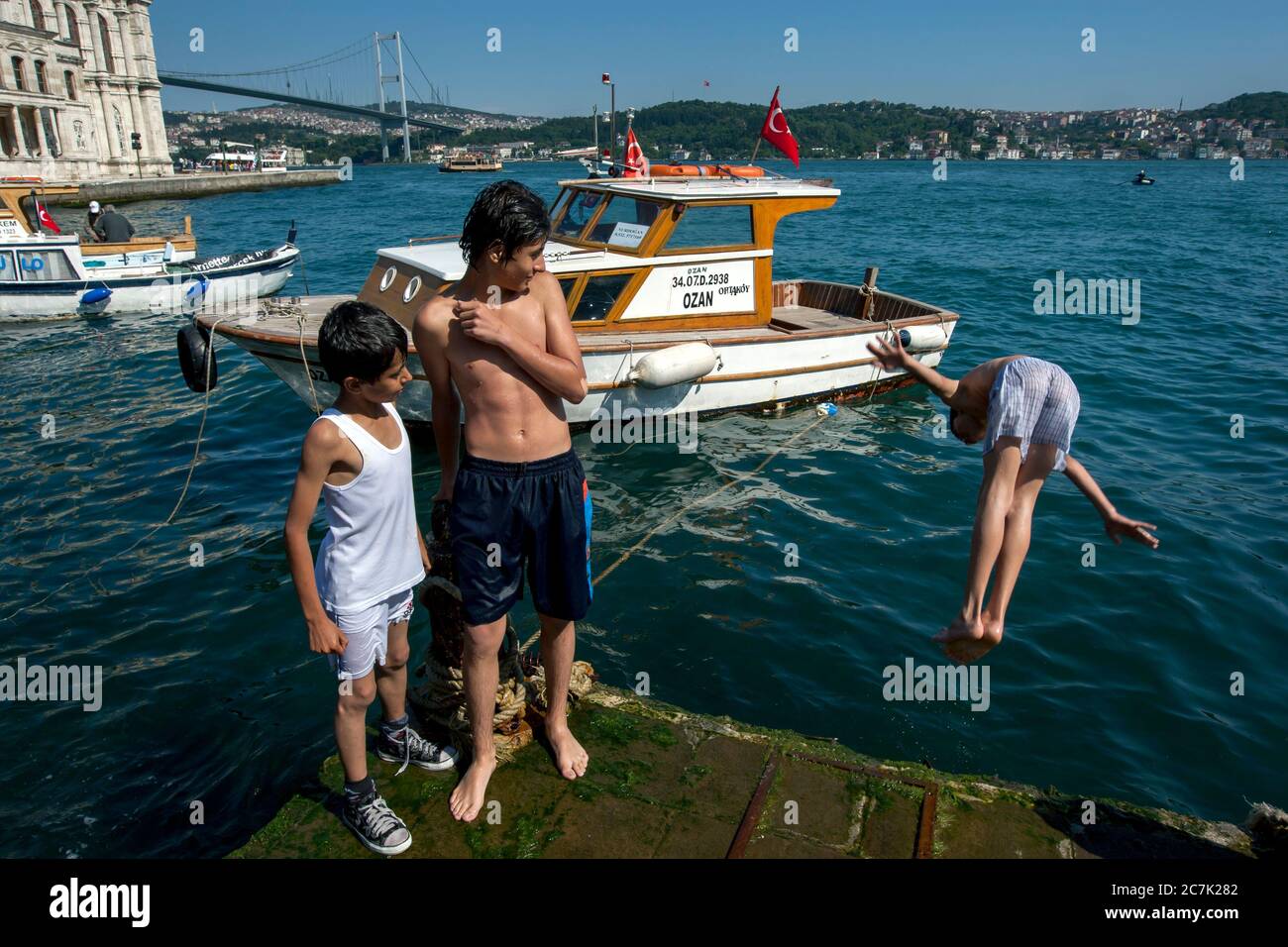 Türkische Jungs kühlen sich an einem heißen Sommertag ab, indem sie von einem Kai in den Bosporus im türkischen Ortakoy-Viertel in Istanbul tauchen. Stockfoto