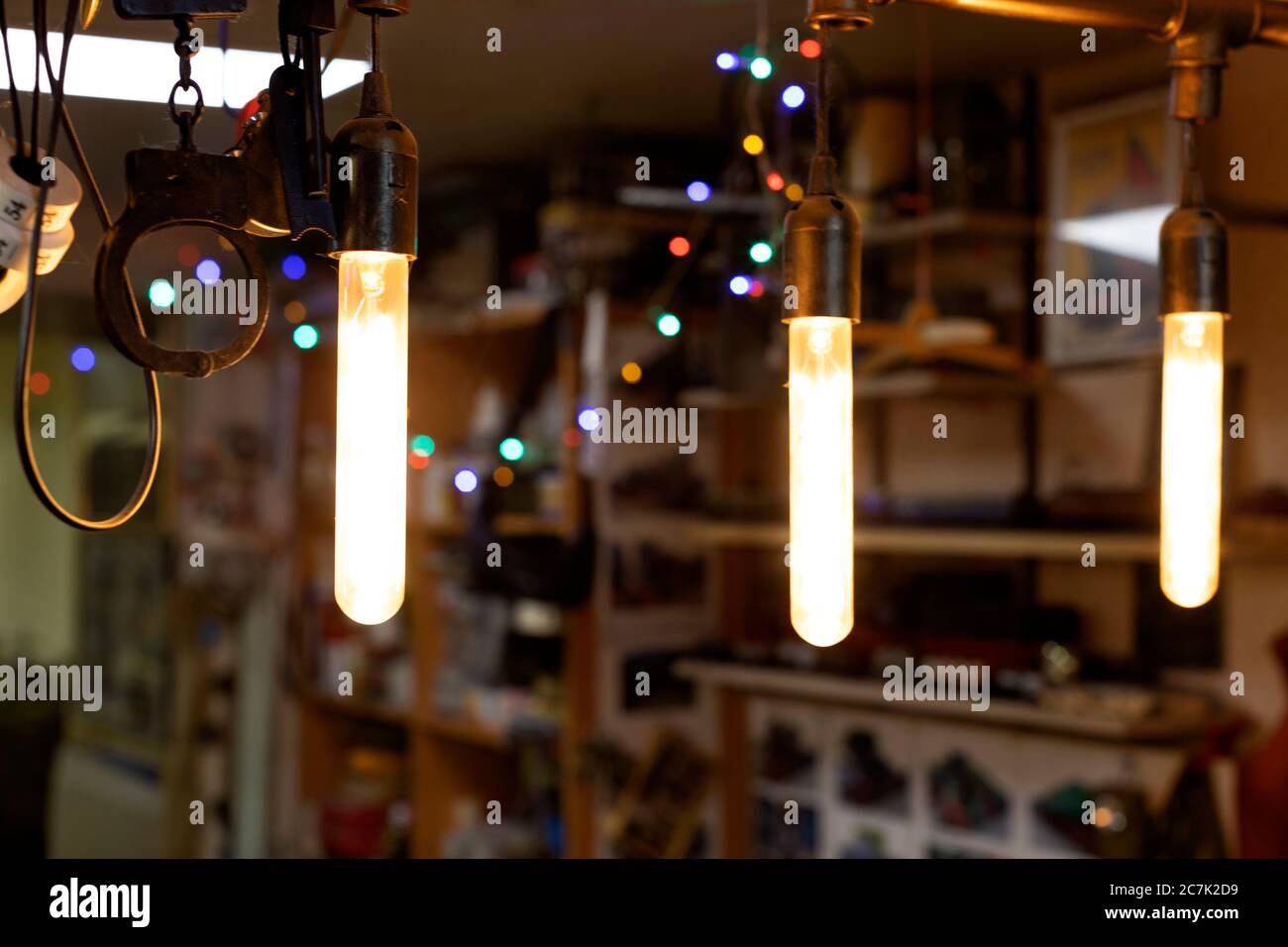 Drei leuchtende längliche Lampen und Handschellen hängen an einem festlichen Ort, mit bunten Lichtern in der Bokeh-Zone Stockfoto
