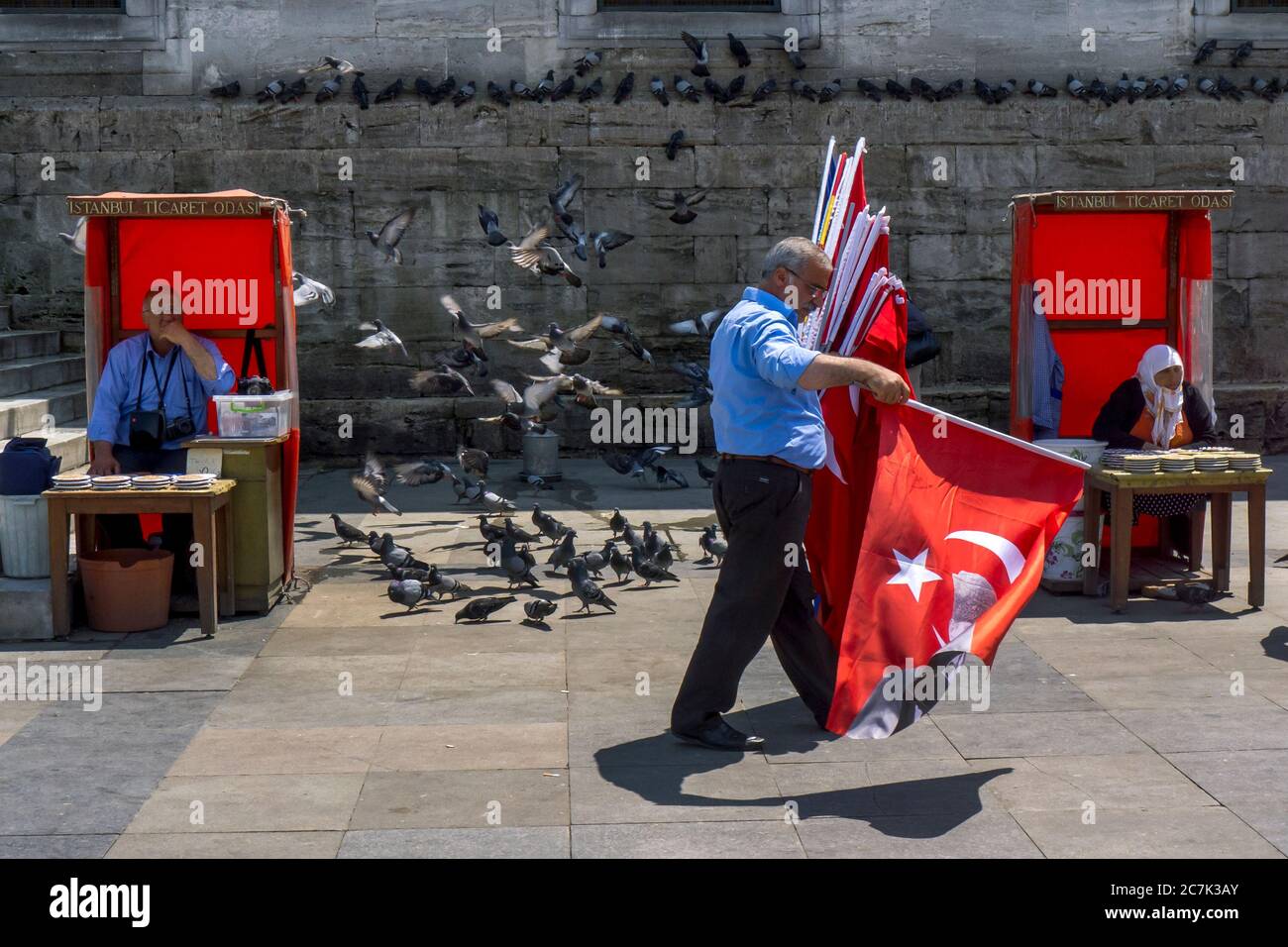 Ein türkischer Flaggenverkäufer kommt an Yeni Camii in Eminonu in Istanbul vorbei. In den Kabinen werden Getreideplatten verkauft, um die Tauben zu füttern. Stockfoto