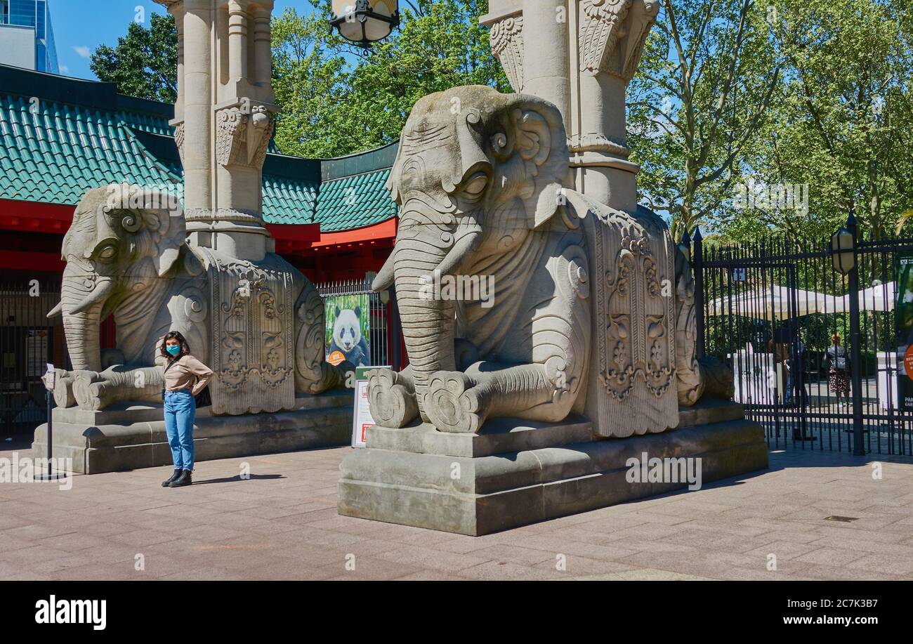 Berlin, Deutschland, 6. Mai. 2020: Eingang des Berliner Zoos mit Skulpturen von Steinelefanten und einer jungen Frau mit Gesichtsmaske Stockfoto