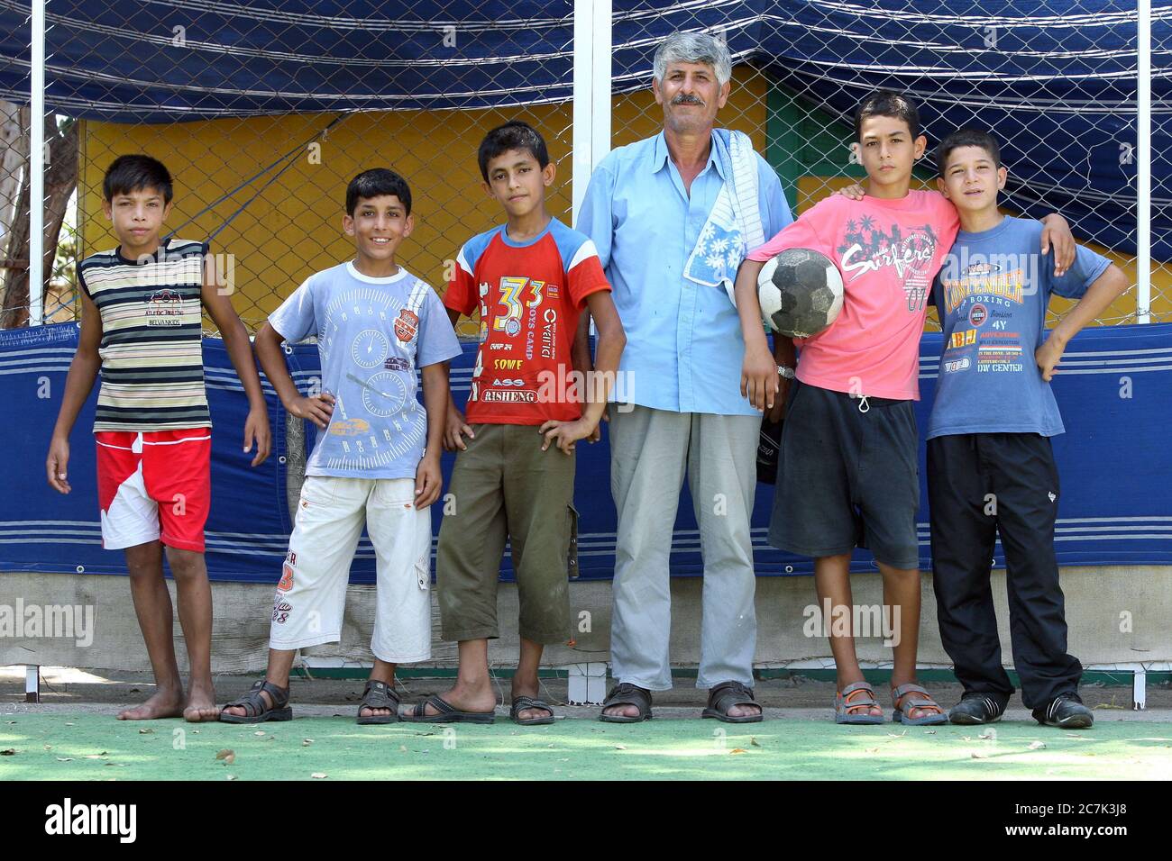 Ein Mann mit einer Gruppe von Jungen, die an einem heißen Sommertag in der türkischen Küstenstadt Mersin Fußball gespielt haben. Stockfoto