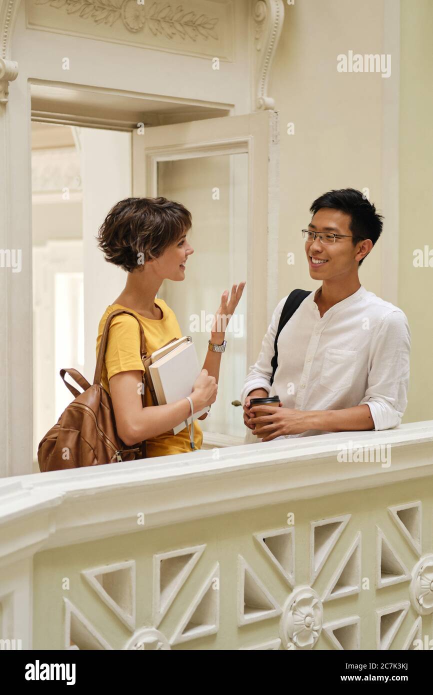 Zwei junge lächelnde internationale Studenten, die in der Pause im Korridor der Universität fröhlich reden Stockfoto
