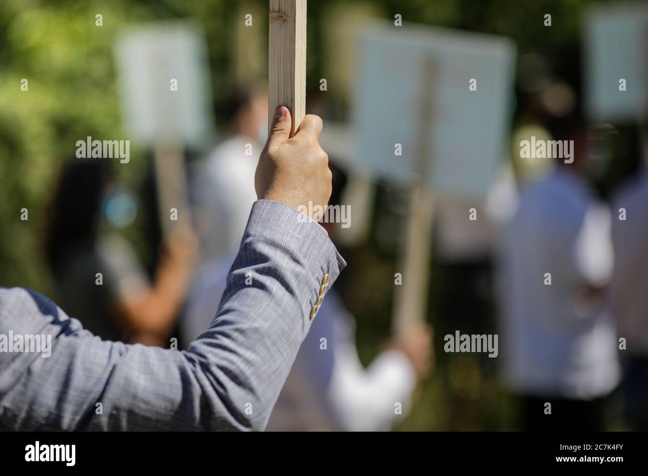 Geringe Schärfentiefe (selektiver Fokus) Bild mit der Hand eines Mannes, der während einer politischen Kundgebung ein Holzplakat hält. Stockfoto