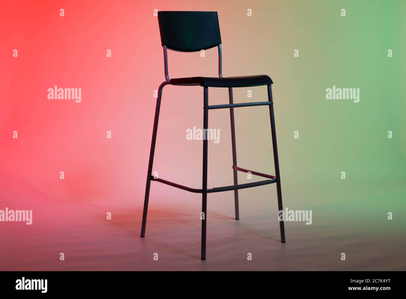 Ein hoher Stuhl steht in einem Fotostudio auf einem weißen Papierhintergrund, der in rot-grünen Tönen leuchtet Stockfoto