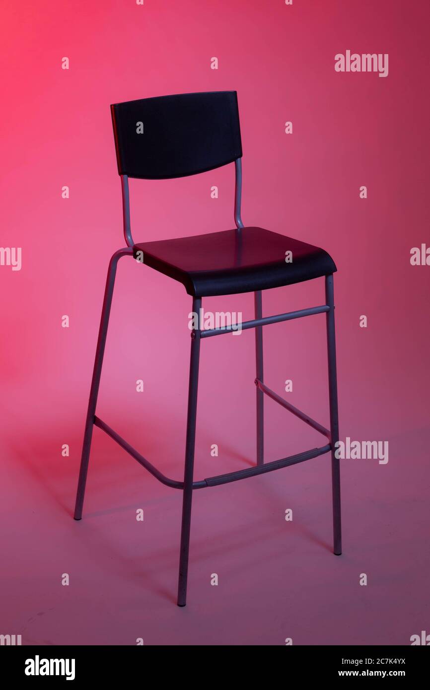 Ein hoher Stuhl steht in einem Fotostudio auf einem weißen Papierhintergrund, der in rosa Tönen beleuchtet ist Stockfoto