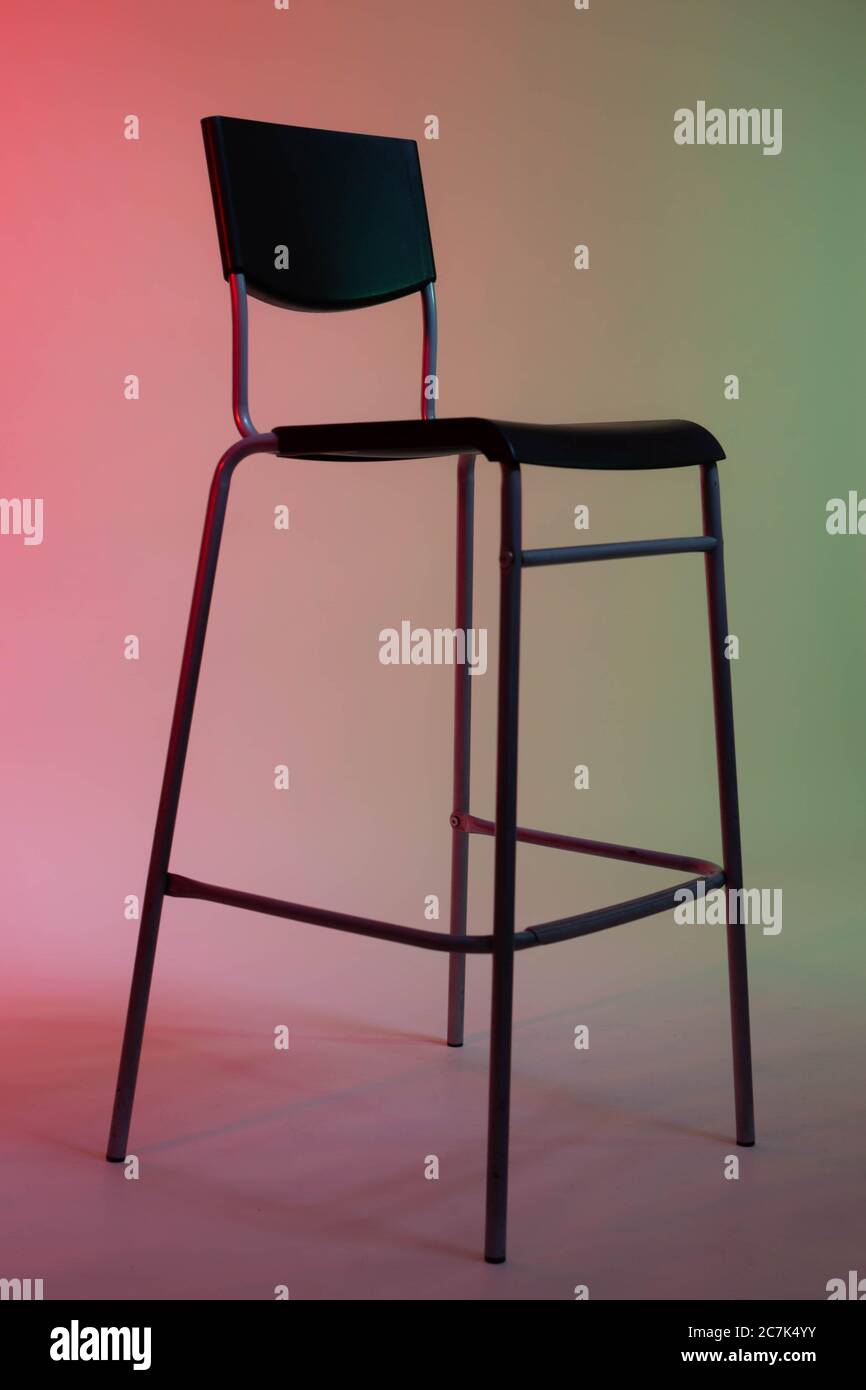 Ein hoher Stuhl steht in einem Fotostudio auf einem weißen Papierhintergrund, der in rot-grünen Tönen leuchtet Stockfoto