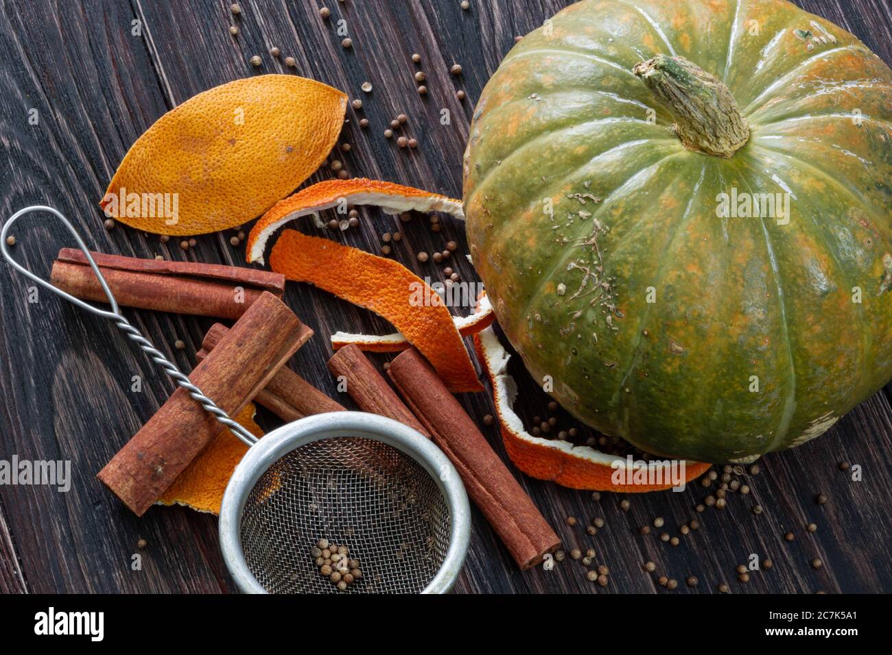 Zimt, Orangenkrusten, Gewürze, Metallsieb und reifer Kürbis auf einem Holztisch Stockfoto