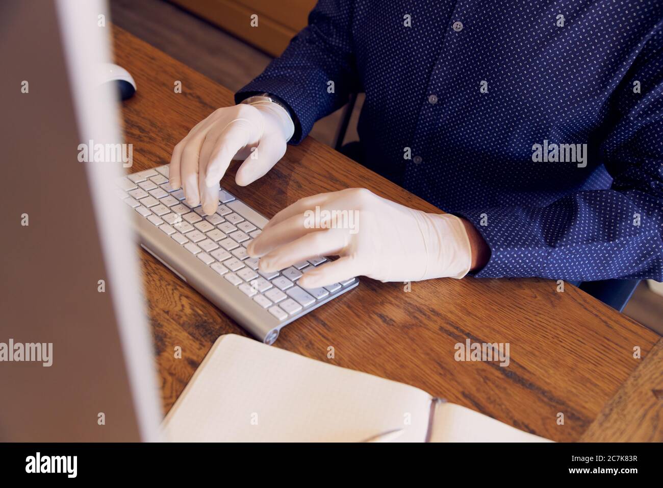 Anonymer Geschäftsmann, der am Schreibtisch arbeitet und Schutzhandschuhe trägt, die auf der Tastatur tippen. Stockfoto