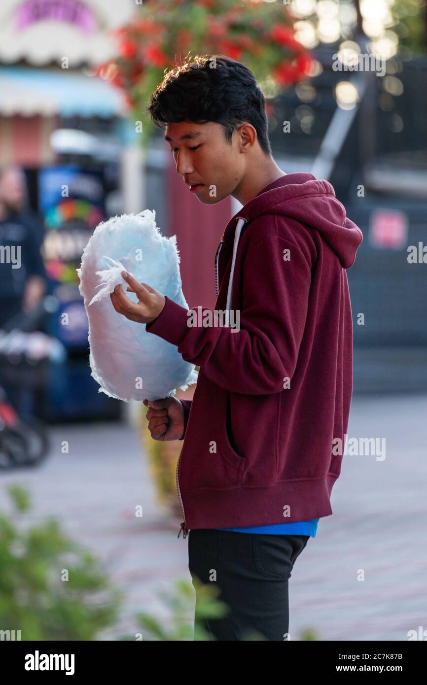 Junger Mann in einem Hoodie essen blaue Zuckerwatte Stockfoto