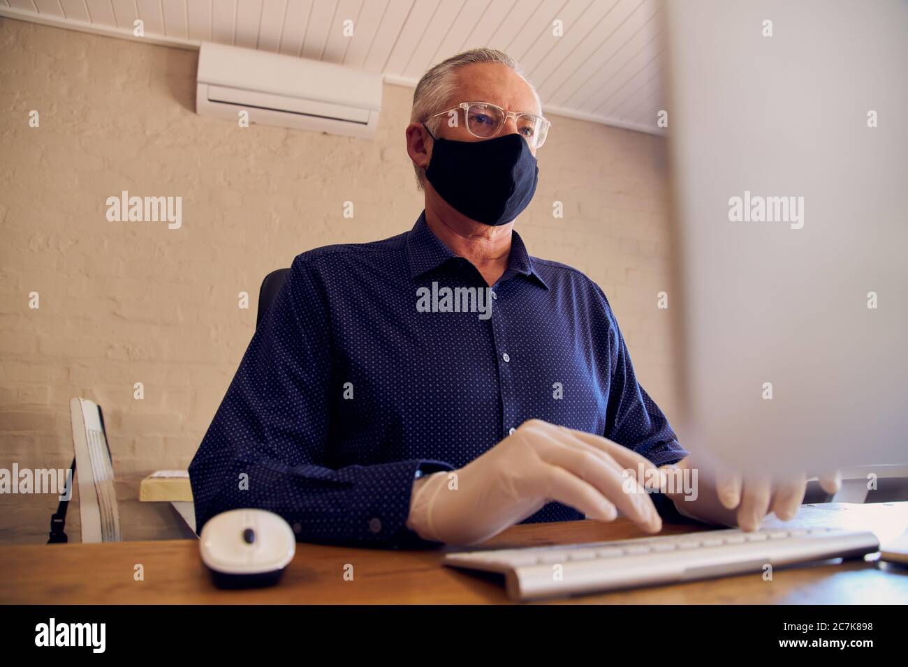 Geschäftsmann, der am Schreibtisch arbeitet und eine Gesichtsmaske vor dem Computer trägt. Stockfoto