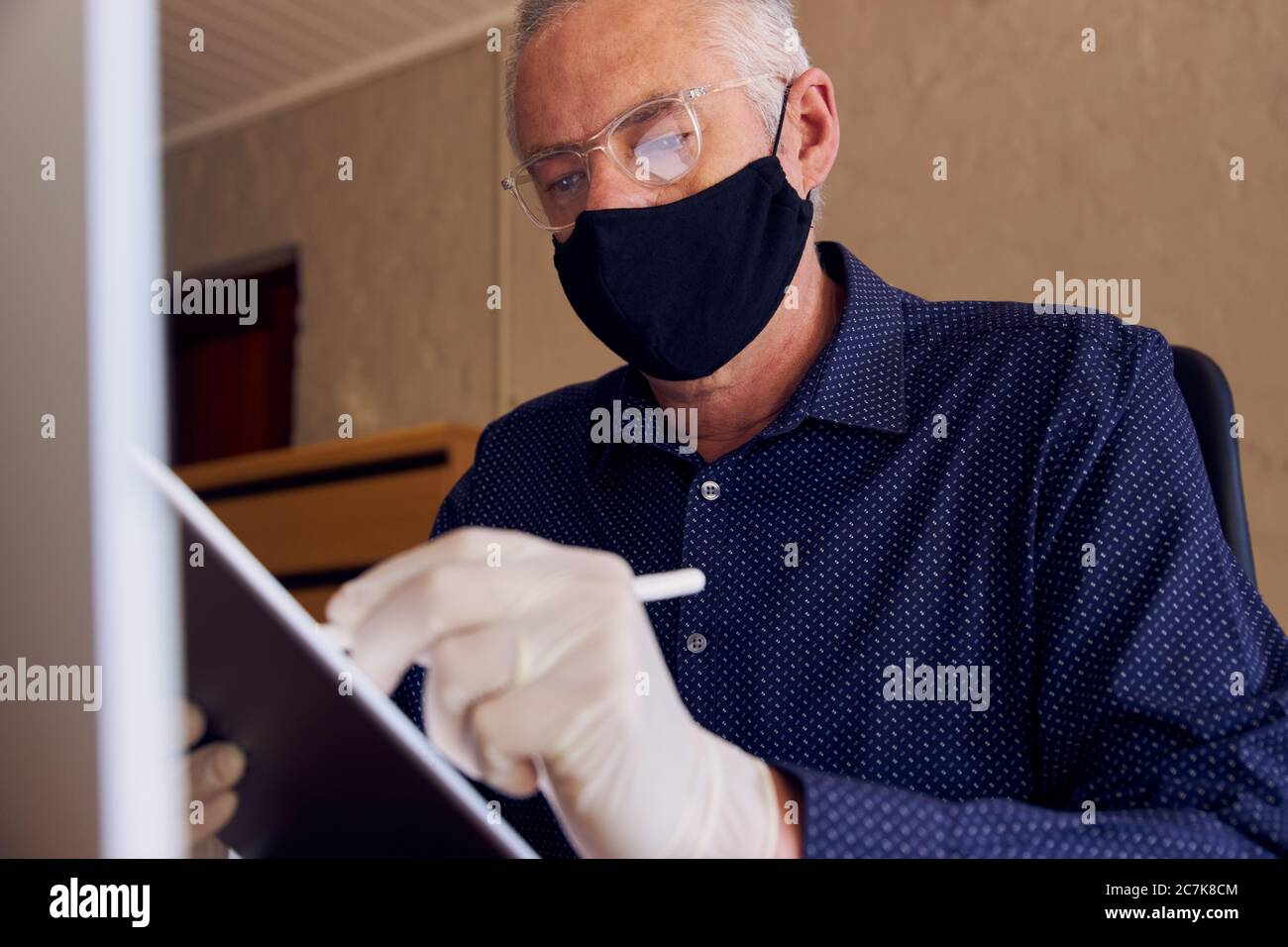 Geschäftsmann, der am Schreibtisch arbeitet und eine Gesichtsmaske auf einem Tablet-Computer trägt. Stockfoto