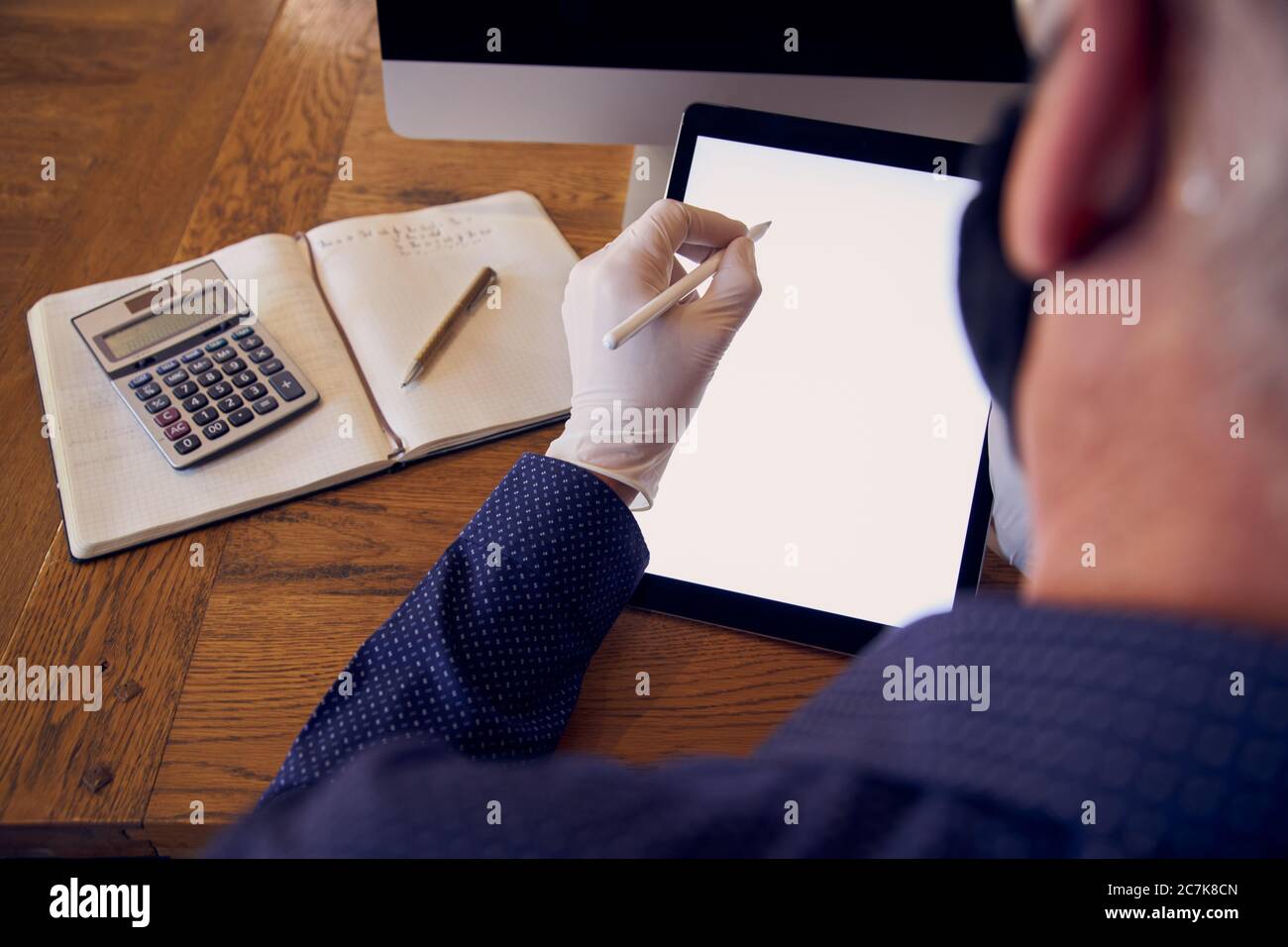Geschäftsmann, der am Schreibtisch arbeitet und eine Gesichtsmaske auf einem Tablet-Computer trägt. Stockfoto