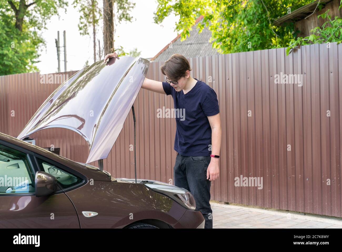 Junger Mann schaut unter die Motorhaube eines Autos in Ratlosigkeit. Auto Zusammenbruch Stockfoto