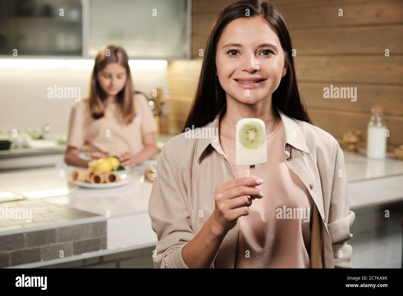 Brunette junge lächelnde Frau zeigt Ihnen hausgemachte eskimo Eis mit frischen Kiwi beim Essen vor der Kamera in der Küche Stockfoto